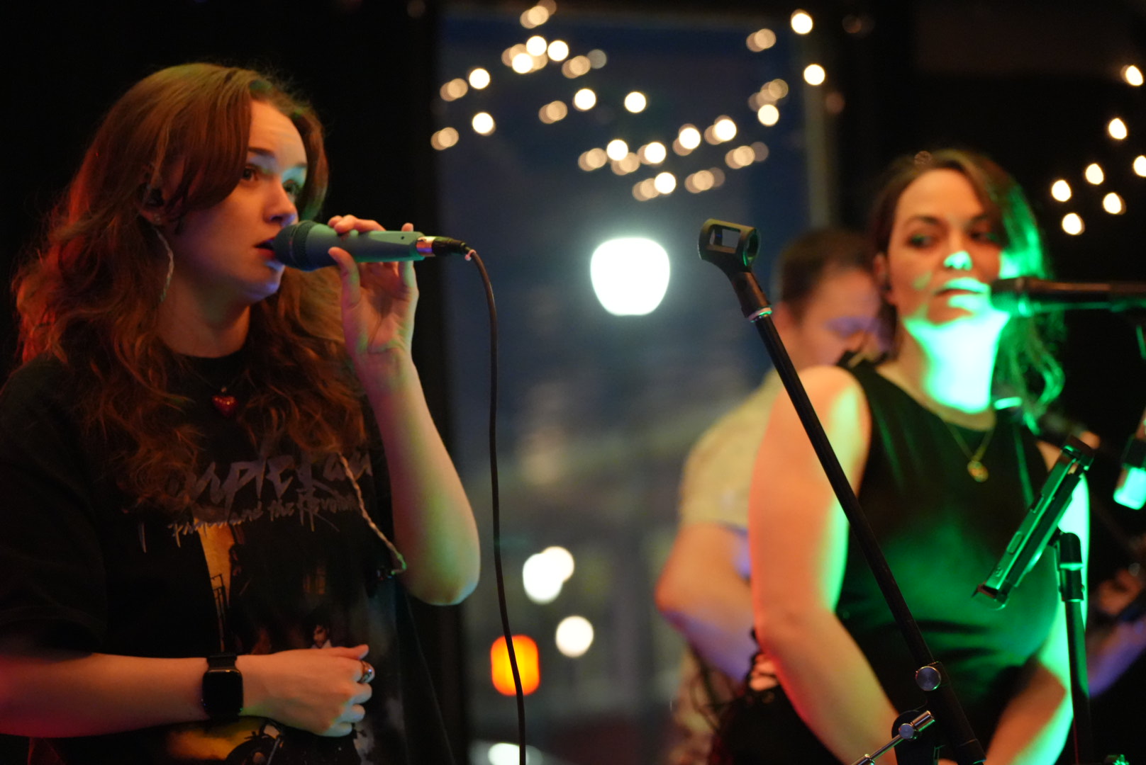 Two vocalists performing under string lights